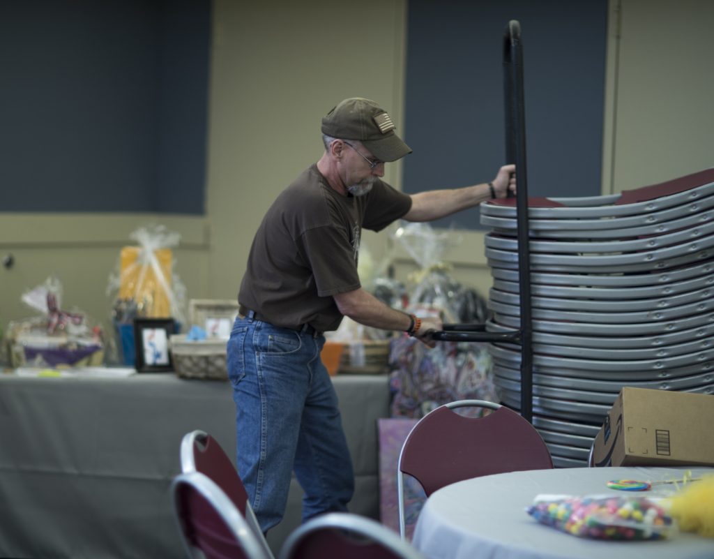 Volunteer moving stacked chairs while setting up an event space